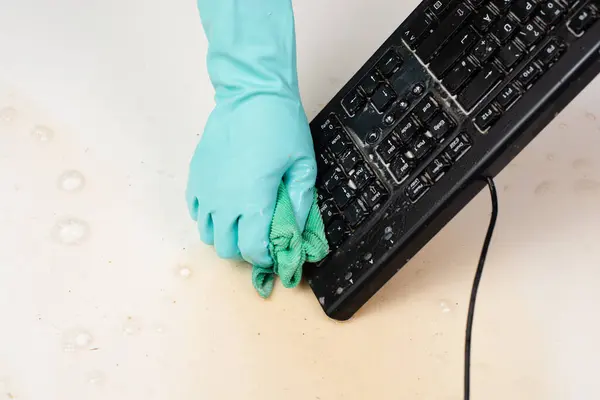 Cleaning computer keyboard in office with rubber protective glove, whiping with water and soap, cleaning dusty and dirty electronic, housework
