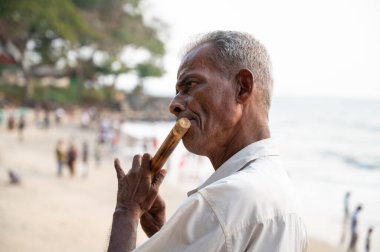 Hindistan 'ın Kochi plajında flüt çalan Hintli adam Vasco da Gama' da müzisyen, sokak müziği, 18.03.2025