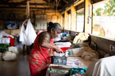 Geleneksel giysili kadın antika bir kömür ütüsüyle, Dhobi Ghat, Kochi, Hindistan 'da hava çamaşırları, 29.03.2025