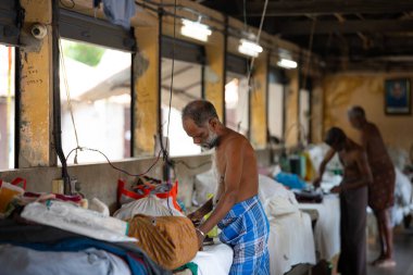 Geleneksel Hint elektrikli ütüsüyle çalışan adam, Dhobi Ghat, Kochi, Hindistan 'da açık hava çamaşırları, eski ütü aletleri, 29.03.2025