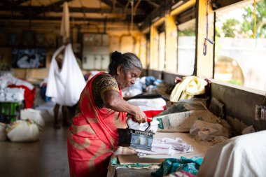 Geleneksel giysili kadın antika bir kömür ütüsüyle, Dhobi Ghat, Kochi, Hindistan 'da hava çamaşırları, 29.03.2025