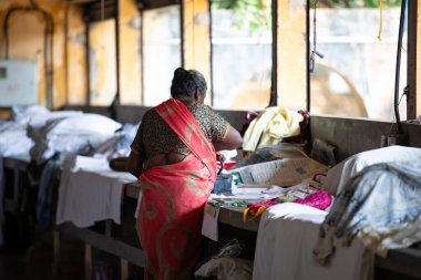 Geleneksel giysili kadın antika bir kömür ütüsüyle, Dhobi Ghat, Kochi, Hindistan 'da hava çamaşırları, 29.03.2025