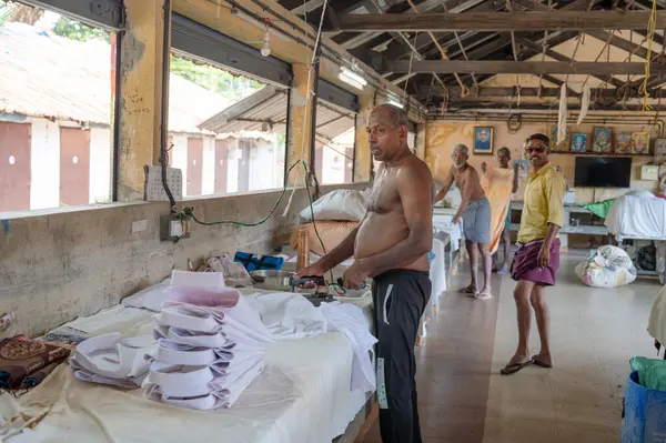 Geleneksel Hint elektrikli ütüsüyle çalışan adam, Dhobi Ghat, Kochi, Hindistan 'da açık hava çamaşırları, eski ütü aletleri, 29.03.202