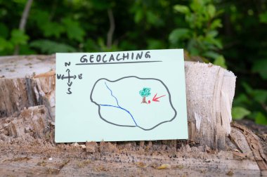 Geocaching, açık hava eğlencesi, saklanıp konteynır aramak için yön bulma, ormandaki geocache konumu, hazine avı oyunu, ağaç gövdesine not.