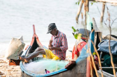Balıkçı teknesiyle geleneksel balık ağını onarıyor, Kochi, Hindistan plajı, Arap deniz kıyısında sanayi, 20.03.2025