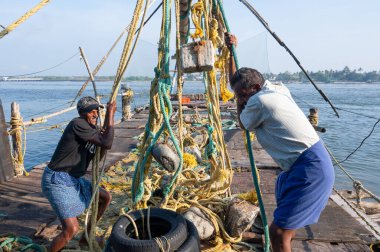 Hindistan 'da Kochi, Kerala, Cheenavala veya Tangkul kıyılarındaki Çin balıkçı ağları, balıkçılar 20.03.2025 geleneksel sabit kaldırma ağından taşlar kaldırıyor.