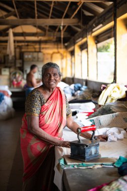 Geleneksel giysili kadın antika bir kömür ütüsüyle, Dhobi Ghat, Kochi, Hindistan 'da hava çamaşırları, 29.03.2025