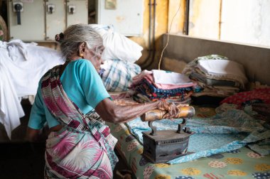 Geleneksel giysili yaşlı kadın antika bir kömür ütüsüyle, Dhobi Ghat, Kochi, Hindistan 'da açık hava çamaşırları, 20.03.2025
