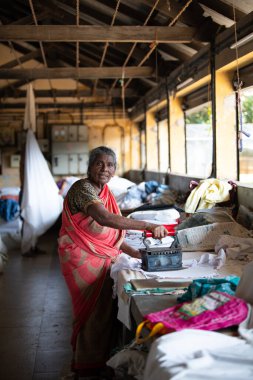 Geleneksel giysili kadın elinde antika bir kömür ütüsüyle, Dhobi Ghat, Kochi, Hindistan 'da 29 Mart 2025' te hava çamaşırhanesini açıyor.