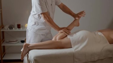 Mumların arka planında SPA salonunda profesyonel bacak masajı. Beyaz üniformalı yakışıklı masör atlet kasları için manüel terapi yapıyor. Sağlık, vücut ve sağlık hizmetleri kavramı.