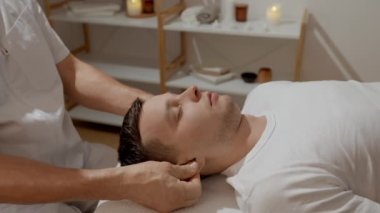 Genç adam, SPA salonundaki profesyonel kafa masajı sırasında dinleniyor. Elle migren tedavisi. Sağlık, vücut ve sağlık hizmetleri kavramı.