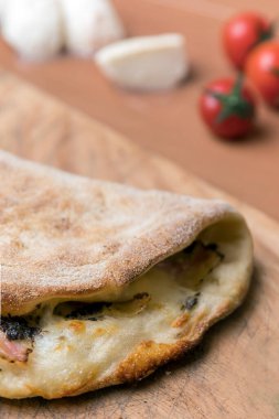 İtalyan yemeği, ahşap arka planda kapalı calzone pizza. Bulanık arka planda küçük kırmızı domatesler ve beyaz mozzarella