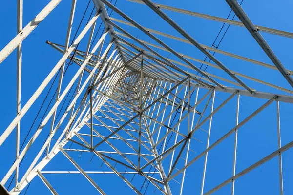 Aşağıdan ve mavi gökyüzünden görülen yüksek voltaj elektrik şebekesi pilonu