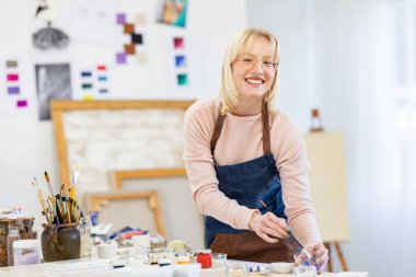 Young woman is in her painting studio. She is posing for the portrait photo of her working there