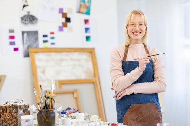 Young woman is in her painting studio. She is posing for the portrait photo of her working there