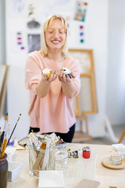 年轻的画家在工作室里拿着装有油漆的瓶子 她站在工作台前 — 图库照片