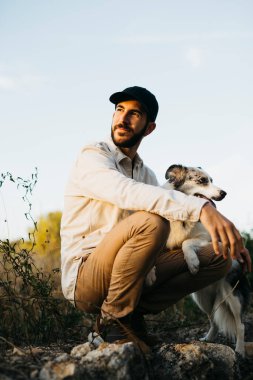 Kırsalda, siyah şapkalı, köpeğiyle birlikte sakallı bir adamın portresi.