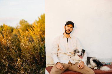 Kırsalda, siyah şapkalı, köpeğiyle birlikte sakallı bir adamın portresi.