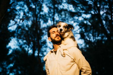 Siyah şapkalı, taşrada sırtında bir köpek taşıyan sakallı bir adamın portresi.