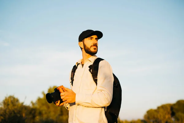 stock image Portrait of a young bearded man, wearing a black cap, with his digital camera at countryside