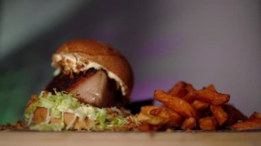 Bacon burger with lettuce accompanied with sweet potatoes on a wooden table and over a black background