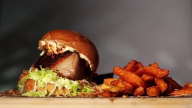 Bacon burger with lettuce accompanied with sweet potatoes on a wooden table and over a black background
