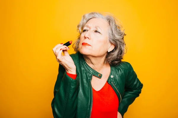 stock image Portrait of a senior woman applying red lipstick over a yellow background