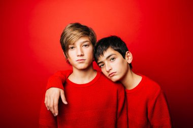 Two Pre-adolescent boys, wearing a red sweater, embracing over a red background clipart