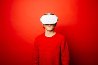 Kırmızı arka plan üzerine kırmızı giyen ergen çocuk sanal gerçeklik gözlükleriyle video oyunları oynuyor.
