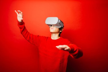 Kırmızı arka plan üzerine kırmızı giyen ergen çocuk sanal gerçeklik gözlükleriyle video oyunları oynuyor.