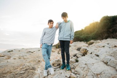 Two male brothers hanging out on a rock breakwater, by the sea