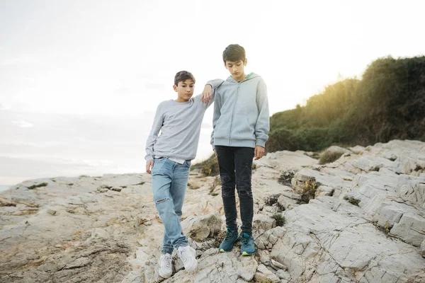 Two male brothers hanging out on a rock breakwater, by the sea