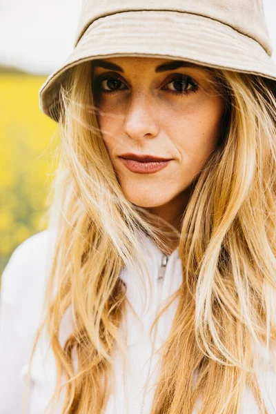 stock image Portrait of a beautiful young blonde cheerful woman, wearing a hat, amidst a field of blooming yellow rapeseed flowers