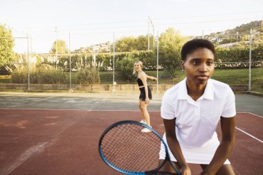 Güneşli bir günde amatör çifte tenis oynayan iki güzel kadın. Tenis kortundaki genç kadın topa vuruyor..