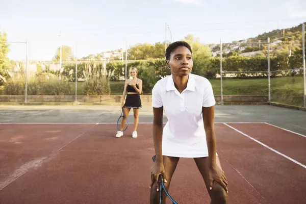 Güneşli bir günde çift tenis oynayan genç ve güzel bir kadının yakın çekimi. Tenis kortunda tenis raketi tutan genç bir kadın maça odaklanıyor..