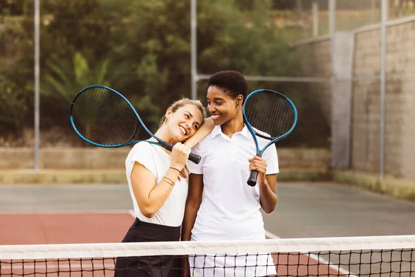 Tenis kortunda tenis kıyafetleri ve raketleri olan ve oyun oynamaya hazır iki güzel kadının portresi..
