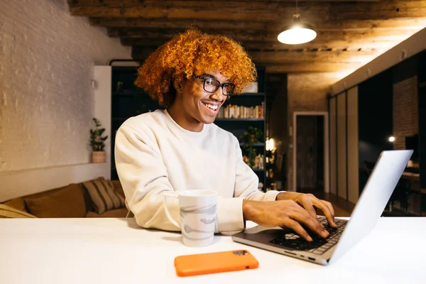 Young african american man typing on a laptop on a kitchen counter in a living room. Happy young man using a laptop at home.