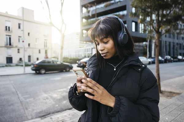 Young woman walking with wireless headphones and using a phone while walking on a city.