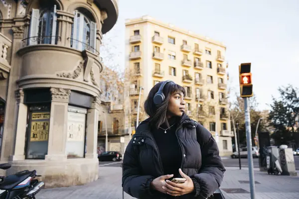 Young woman walking with wireless headphones and a phone while walking on a city.