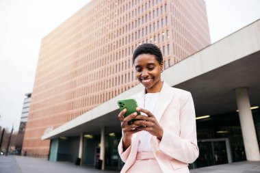 Genç, güzel, gülümseyen bir iş kadını, şehirdeki bir kahve molası sırasında telefonuyla online bir mesaj gönderiyor..