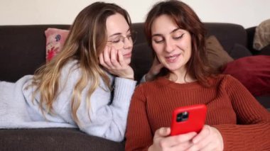 Dişi eşcinsel çift kanepede uzanıyor ve oturma odalarındaki bir telefonda araştırma yapıyorlar. Oturma odasındaki cep telefonunda araştırma yapan iki lezbiyen kadın kanepede uzanır..
