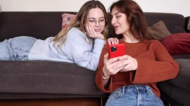 Dişi eşcinsel çift kanepede uzanıyor ve oturma odalarındaki bir telefonda araştırma yapıyorlar. Oturma odasındaki cep telefonunda araştırma yapan iki lezbiyen kadın kanepede uzanır..