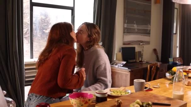 在舒适的厨房里吃早餐的时候 一对快乐的年轻女同性恋者在家里分享着亲吻和亲切的笑话 — 图库视频影像