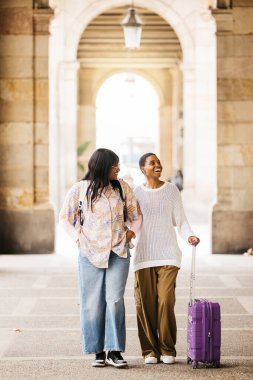 Hafta sonu gezisi sırasında bavul çeken ve şehirde birlikte yürüyen iki neşeli genç kadın..