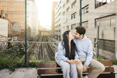 Irklar arası bir çift bankta oturuyor ve şehir manzarasında takılıyorlar. Genç bir adam ve kadın, şehir caddesinde bir demiryolunun üzerinde bir bankta oturuyor..