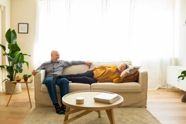 Senior married couple relaxing on a sofa in their living room. Senior couple lying down on a sofa enjoying a peaceful and comfortable moment together at home.
