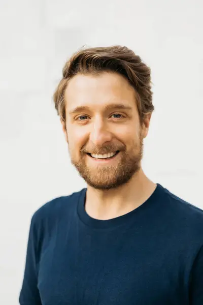 stock image Portrait of a cheerful man standing against a white wall, wearing a blue t-shirt.