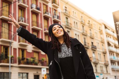Rastalı kadın kolunu yukarı doğru uzatıyor. Şehir caddesinde taksi yakalamaya çalışıyor..