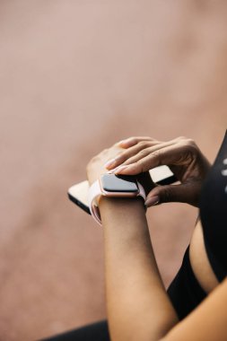 Akıllı saatini ayarlayan, bileğine ve eline odaklanan bir kadının yakın çekimi. Kadın antrenman sırasında sağlık durumunu takip ediyor..