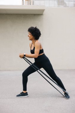 Dışarıda elastik bantla antrenman yaparken gülen genç bir kadın..